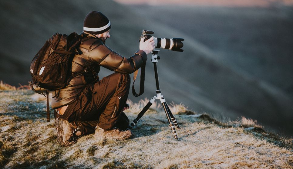 a person taking a picture using a camera and tripod with icey mountains behind