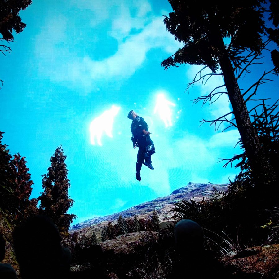 Person floating above a rocky forest clearing, framed by tall trees, with two glowing human-shaped light figures against a bright blue sky.