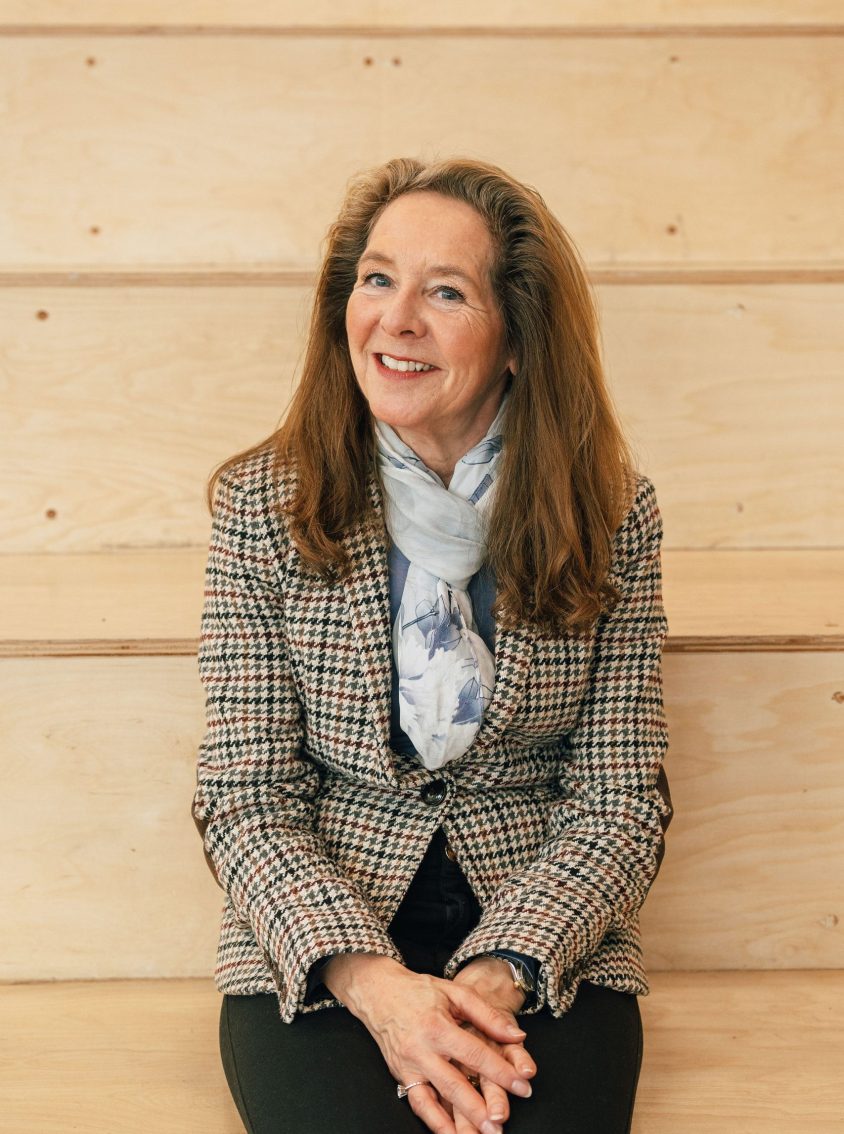 A smartly dressed woman wearing a houndstooth jacket sitting on wooden steps.