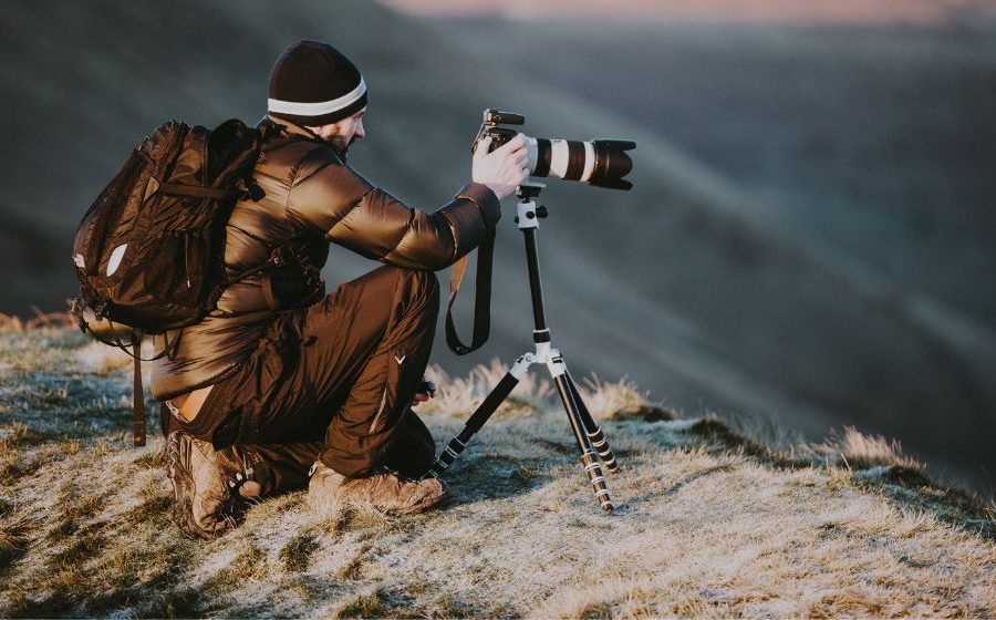 a person taking a picture using a camera and tripod with icey mountains behind