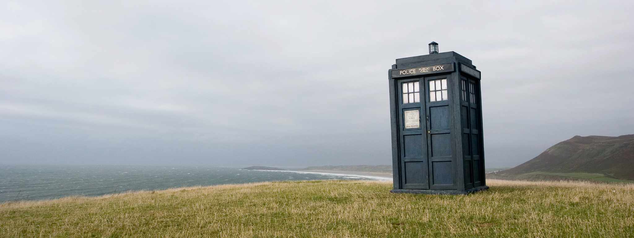 Doctor Who's Police Box Tardis on the headland of Rhossili Bay, with beach and sea behind