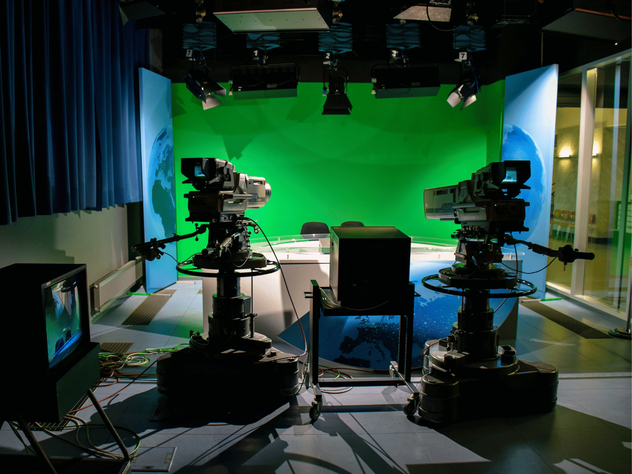 Television cameras pointing at a presenter's desk and greenscreen.
