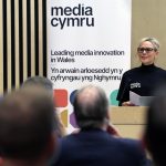 an audience watching a woman present in a lecture theatre. There is a banner in the background which reads Media Cymru - leading media innovation in Wales