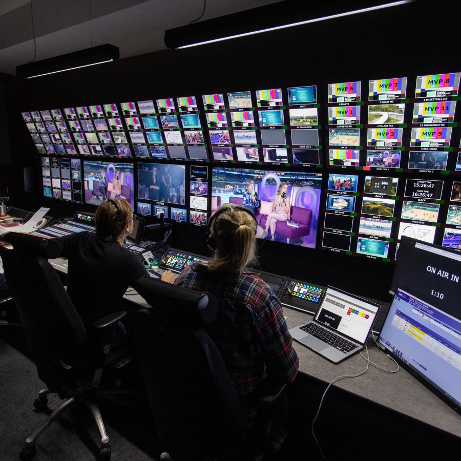 people sitting at desks behind lots of TV screens