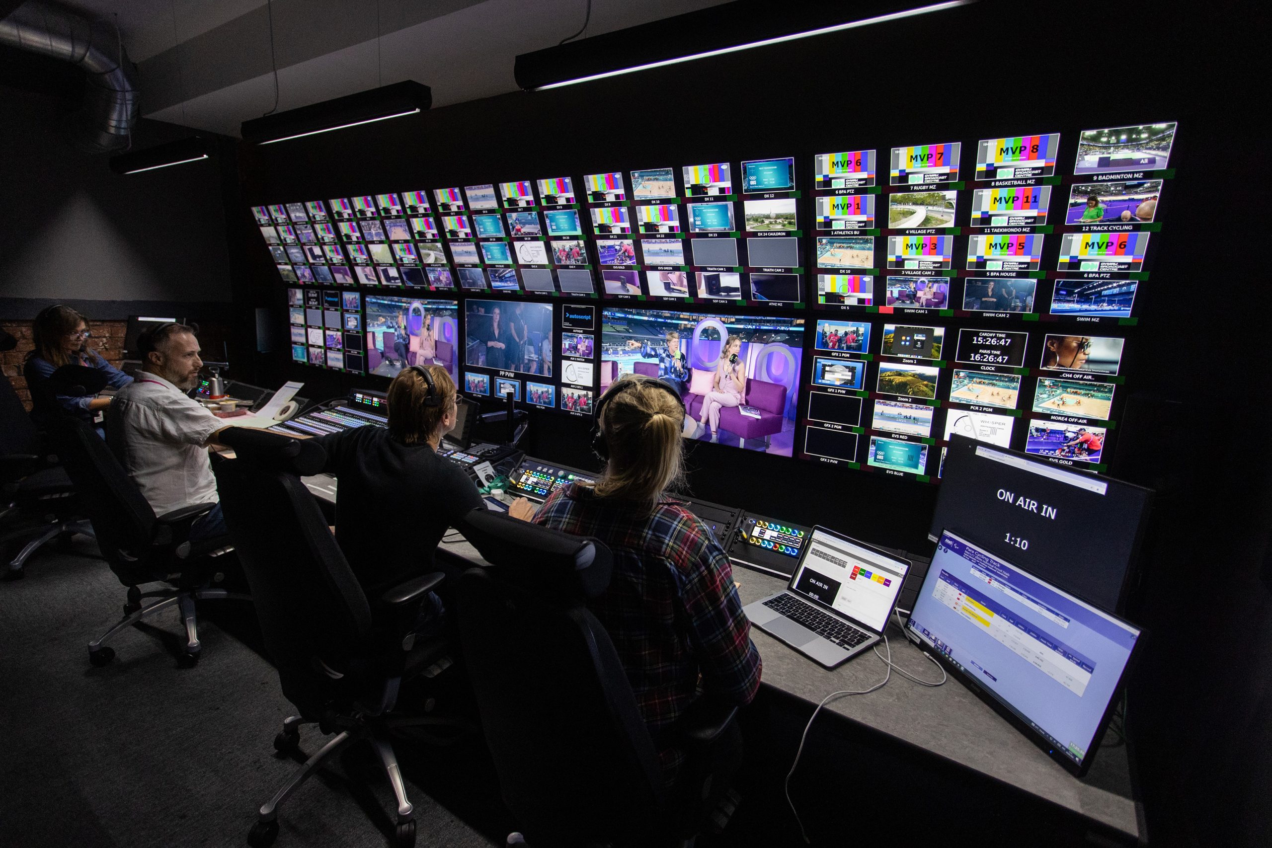 people sitting at desks behind lots of TV screens