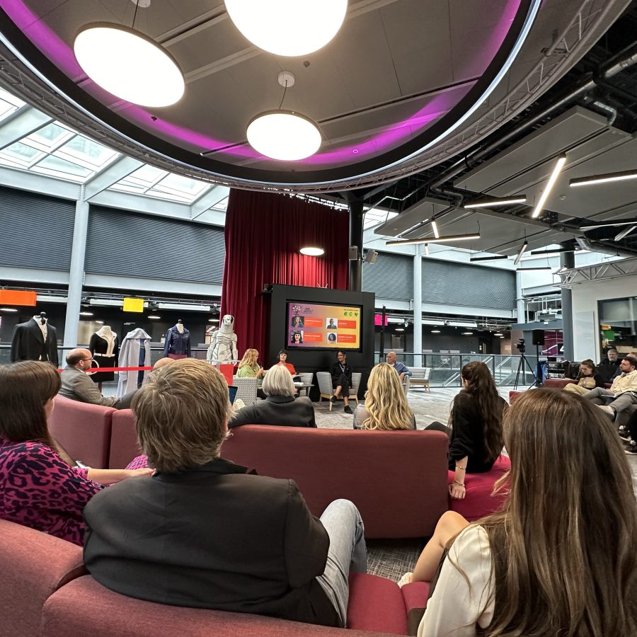 audiences of people sitting on red sofas watching four people sitting on chairs behind a TV screen