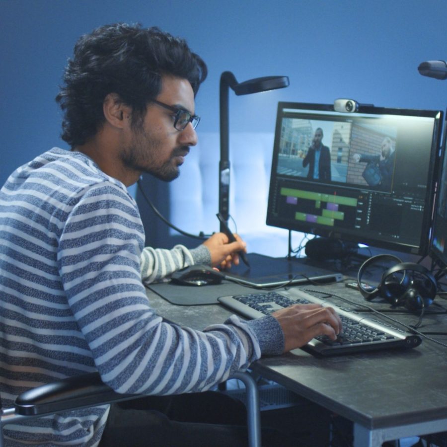 a person in a wheelchair working at a desk at his computer, the wall in the background is blue, the computer and desk is black