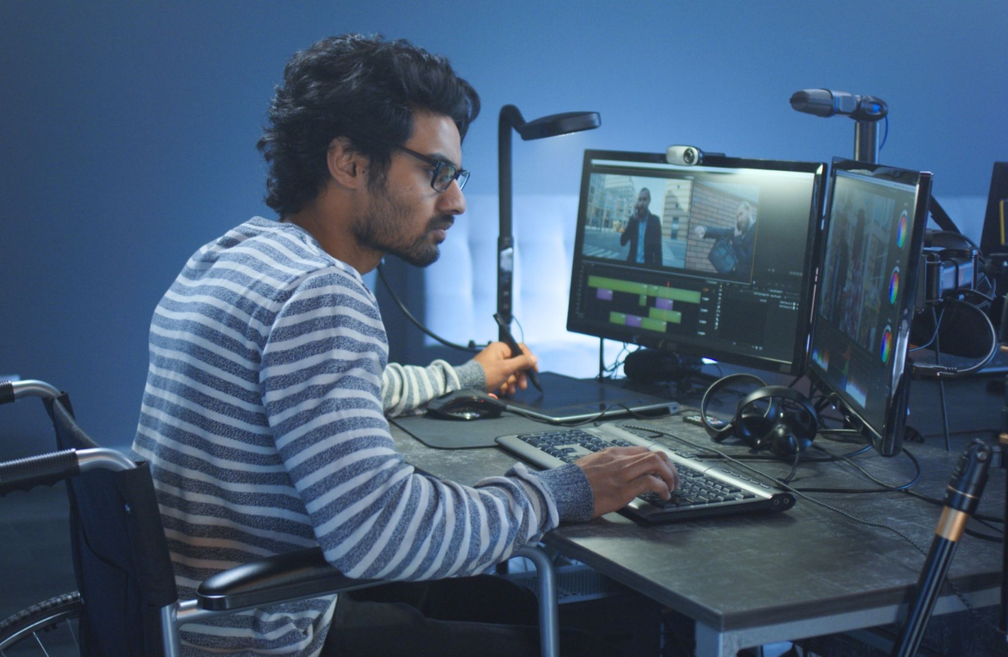 a person in a wheelchair working at a desk at his computer, the wall in the background is blue, the computer and desk is black