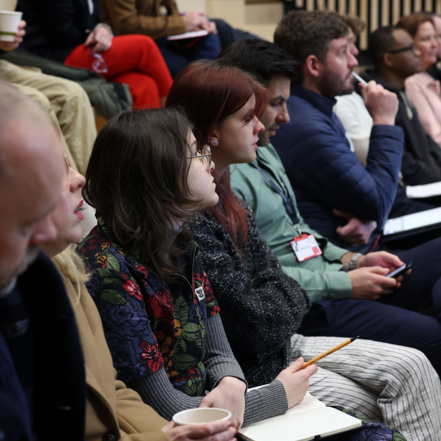 a group of people sitting in a row looking forwards at someone presenting to them, their faces are engaged