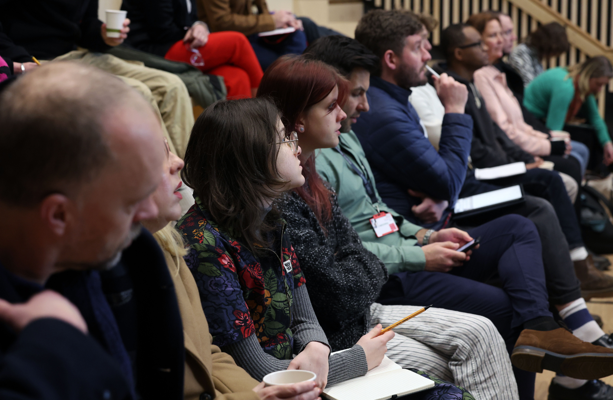 a group of people sitting in a row looking forwards at someone presenting to them, their faces are engaged