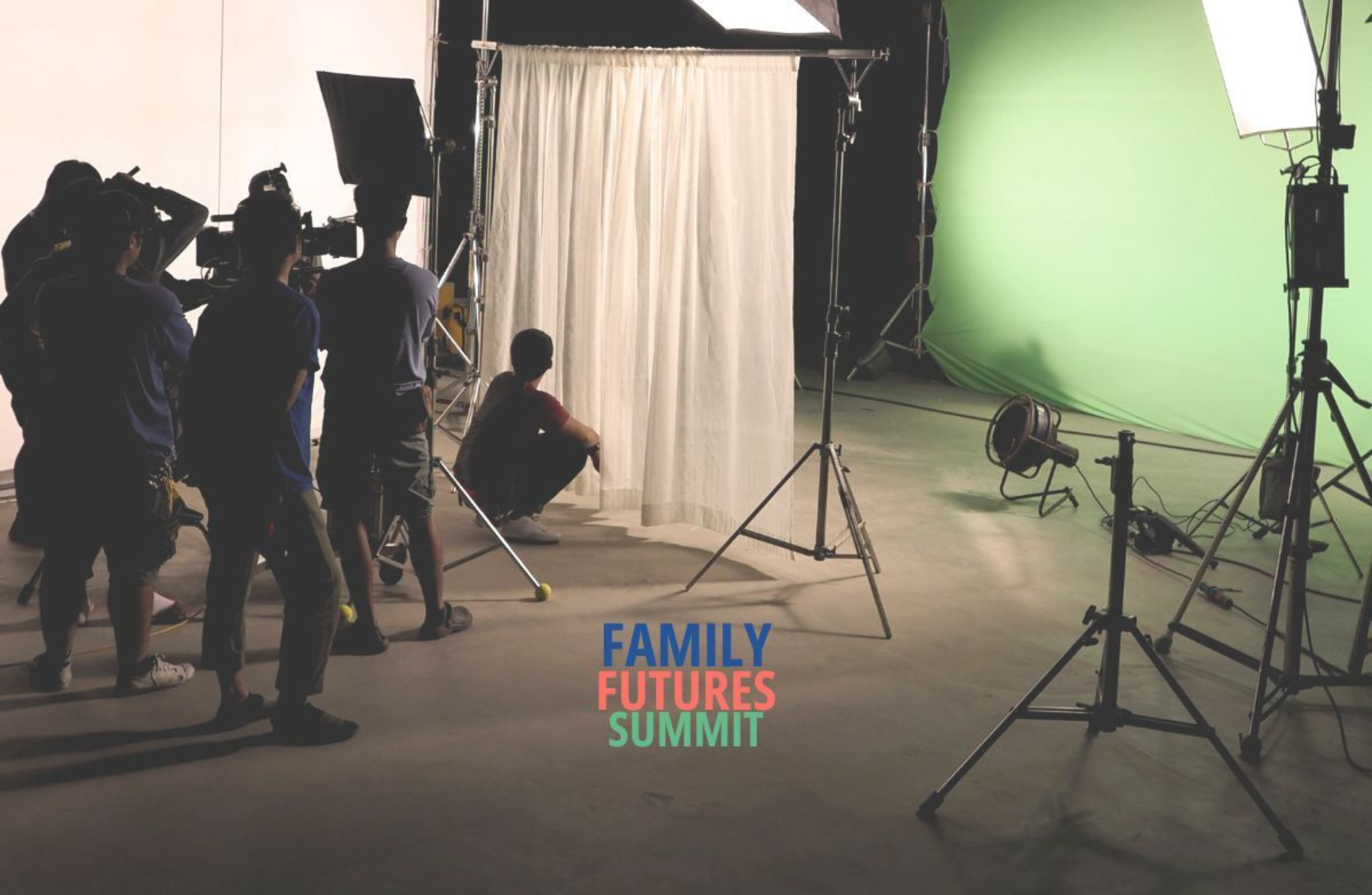 A behind-the-scenes view of a film or photo shoot set. Several crew members are working with cameras and lighting equipment. A person is sitting on the floor near a white curtain backdrop, with a green screen in the background. The text 'FAMILY FUTURES SUMMIT' appears at the bottom centre in blue, red, and green.