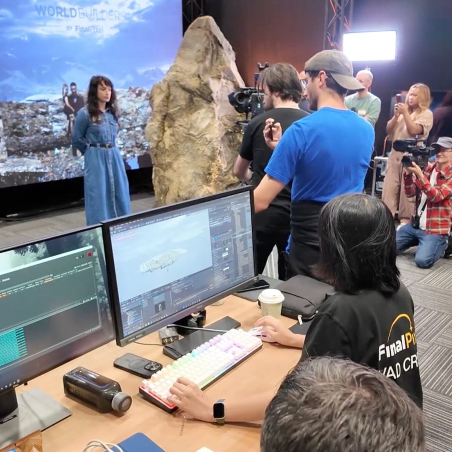 A behind-the-scenes studio scene with cameras, monitors, and crew gathered around a live virtual production demonstration.